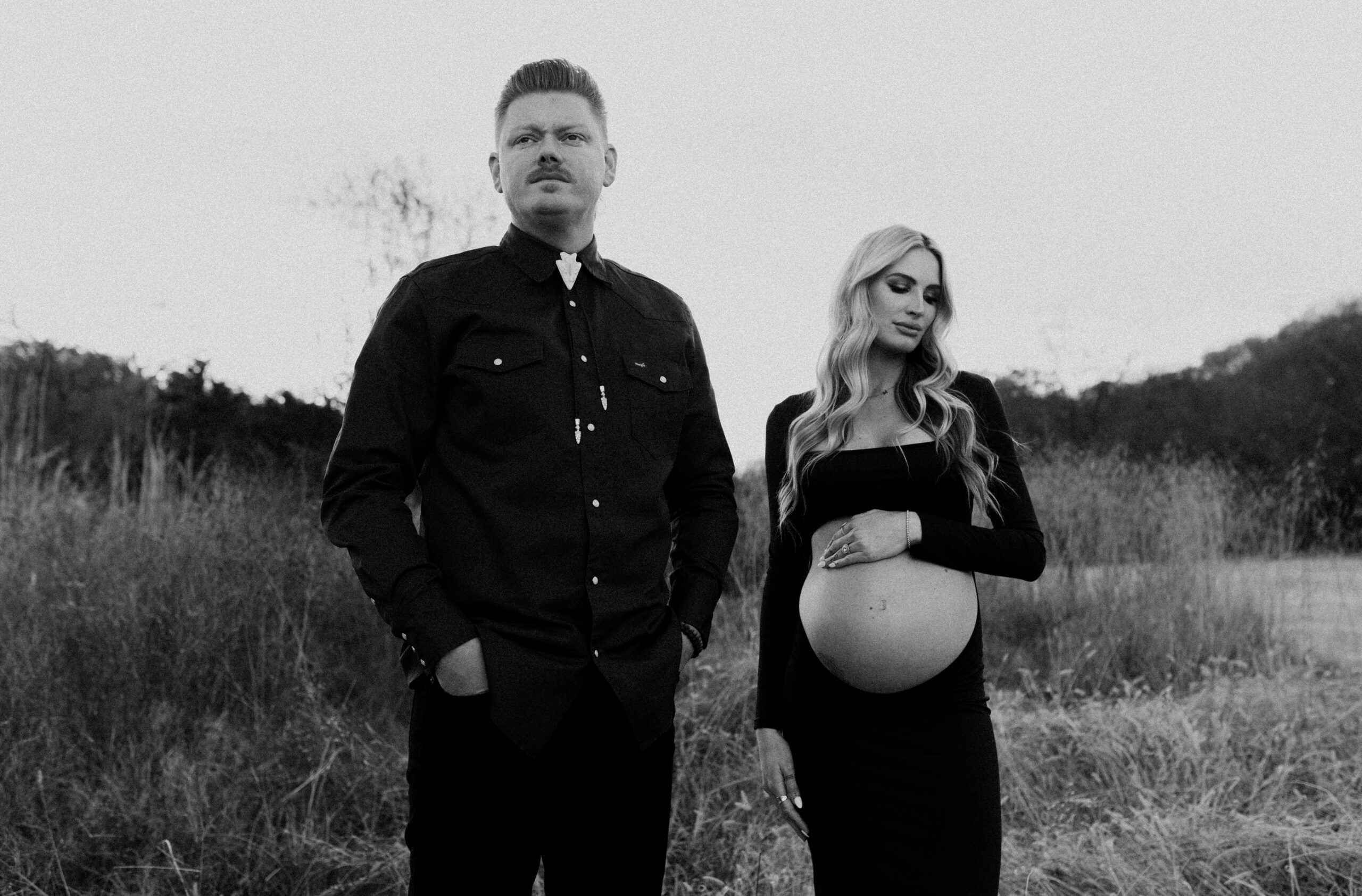 husband and wife standing next to each other in a field with mountains